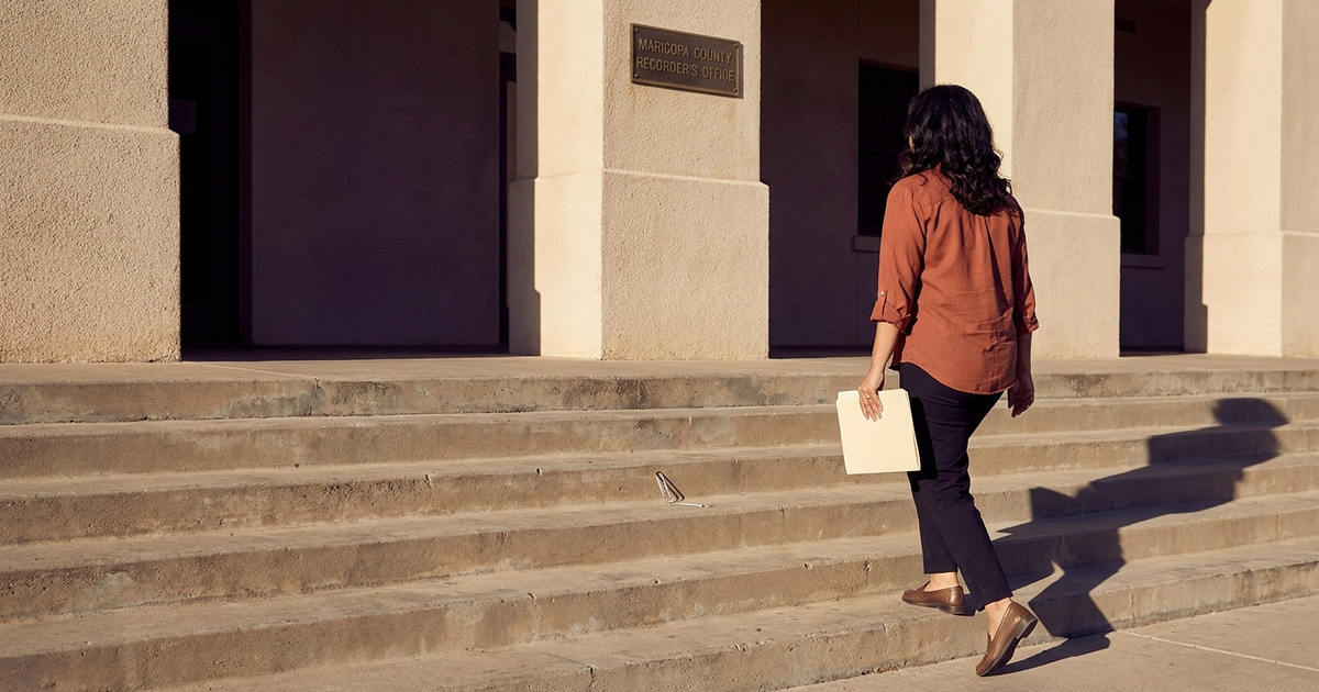 Maria Salgado-Whitman walking up the front steps of the Maricopa County Recorder's office, manila folder in hand, early-morning desert light.